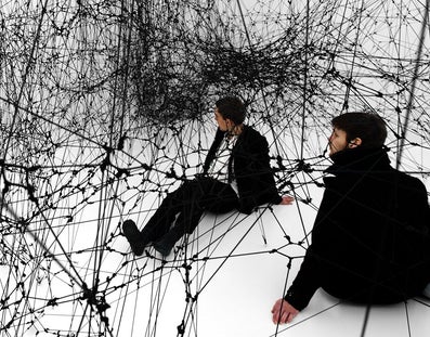  Two men sit in a gigantic black spider web (sculpture by Tomas Saraceno)