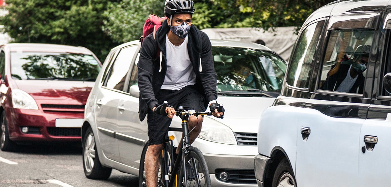 Cyclist bikes with facemasks near cars 