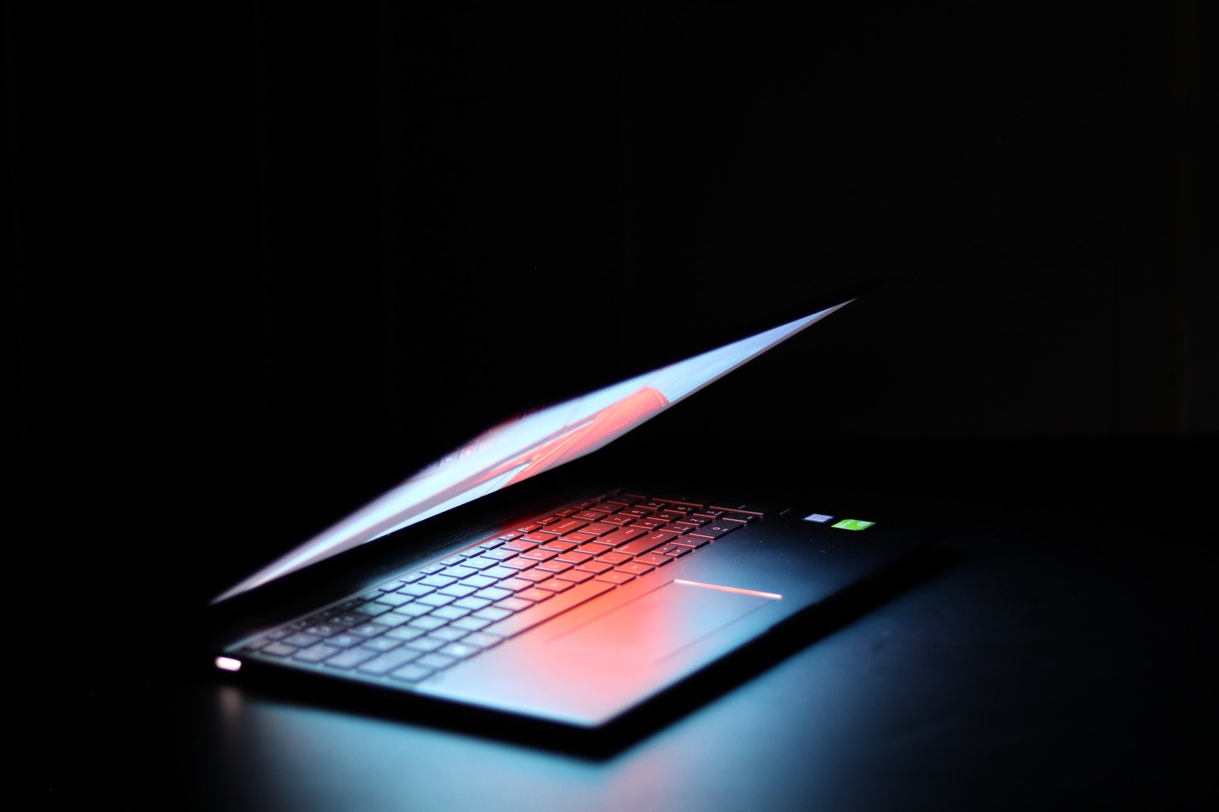 A half-opened laptop in a dark space with only a light shining on the laptop