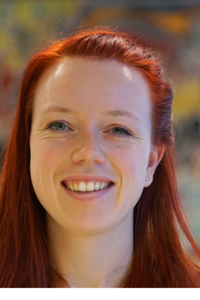 Broad-smiling woman with long red hair against a vaguely colourful background