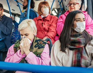 People wearing masks in public transport, one of them is blowing her nose