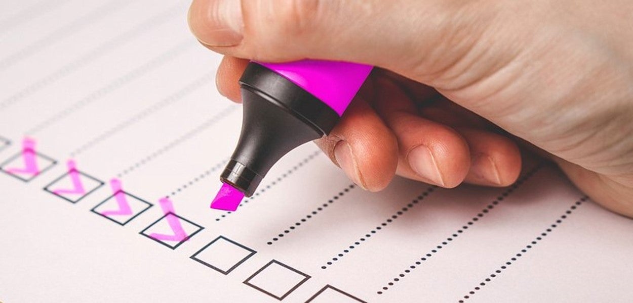 Zijaanzicht van een hand die met roze marker op een checklist schrijft 