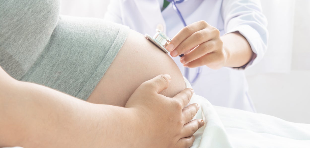 Doctor examines pregnant woman's belly with a stethoscope. 