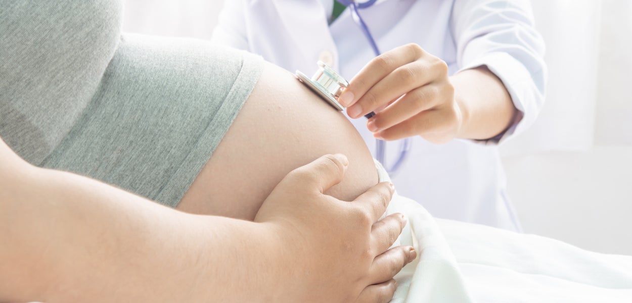 Doctor examines pregnant woman's belly with a stethoscope. 