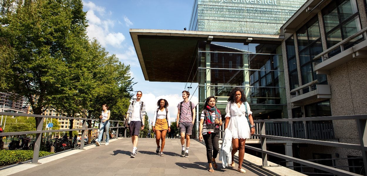 A group of students walking together across a walkway at the entrance to the main building of Vrije Universiteit Amsterdam.