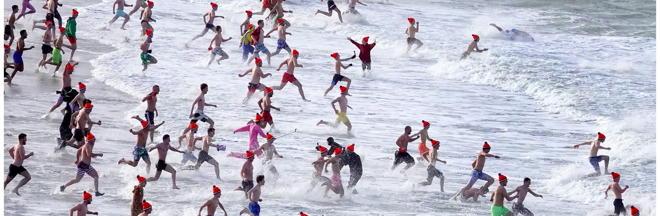 People running into the sea wearing swimwear, with caps on their heads