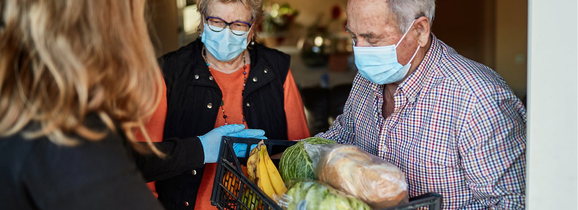 A man and a woman wearing mouth masks, receive a box of groceries