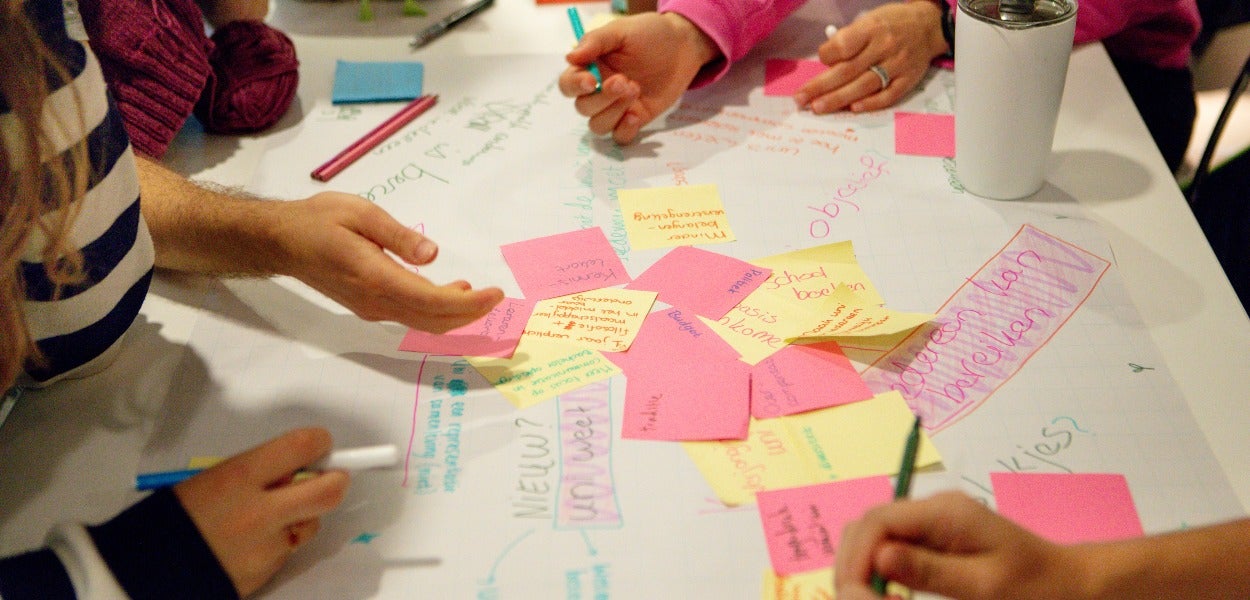 Various people participate in a brainstorming session with colourful post-its and handwritten notes on a large sheet of paper.