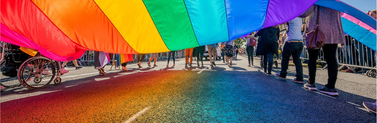 Members of the Pride Walk carry the rainbow flag in the street.