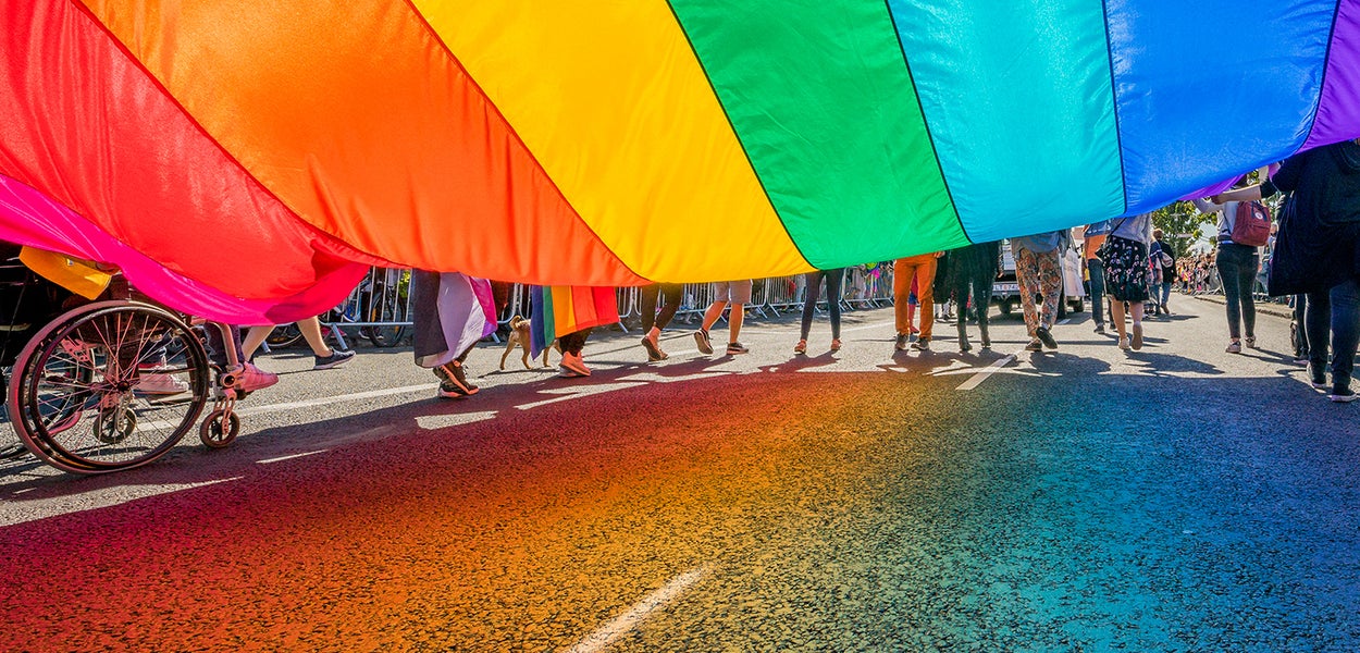 Members of the Pride Walk carry the rainbow flag in the street.