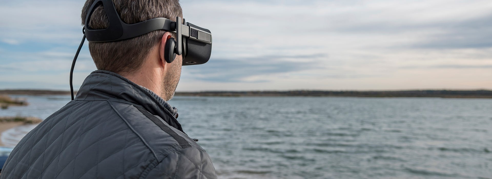 A man looks across the water wearing a VR headset
