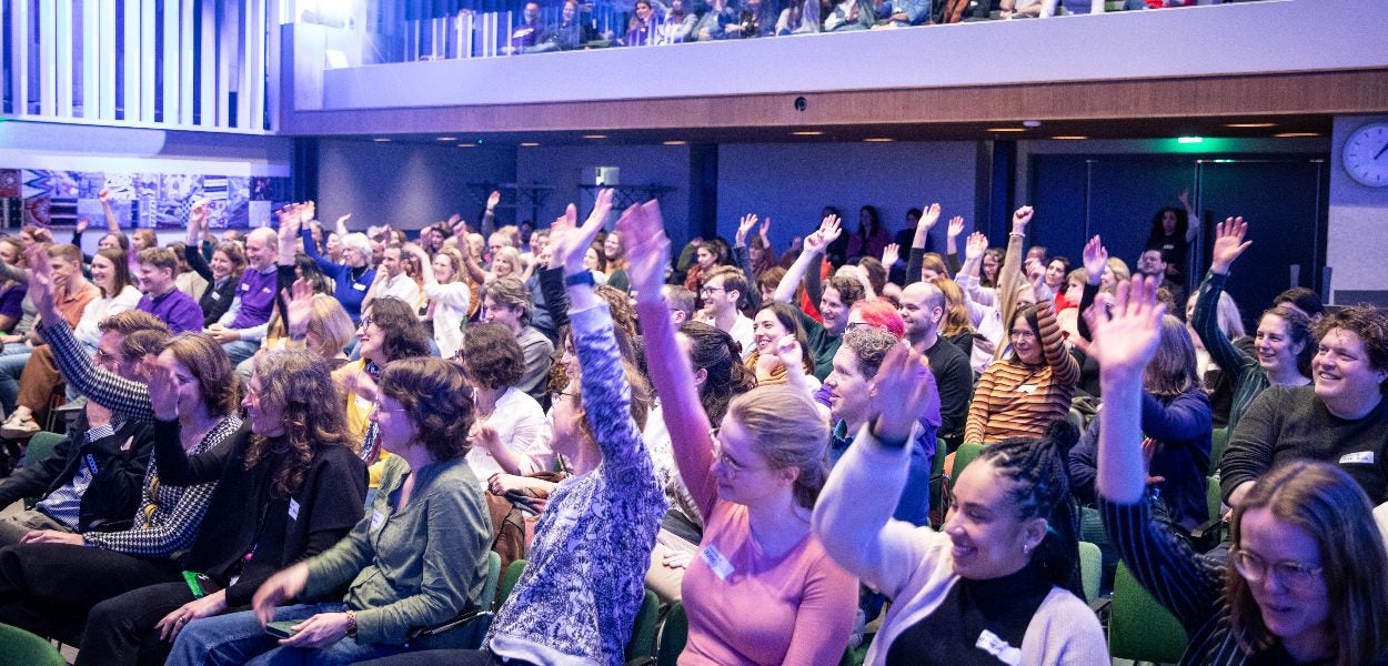An enthusiastic audience raising their hands in a conference hall.