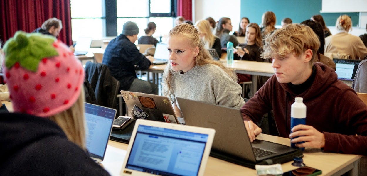 Studenten die geconcentreerd werken op hun laptops in een klaslokaal.