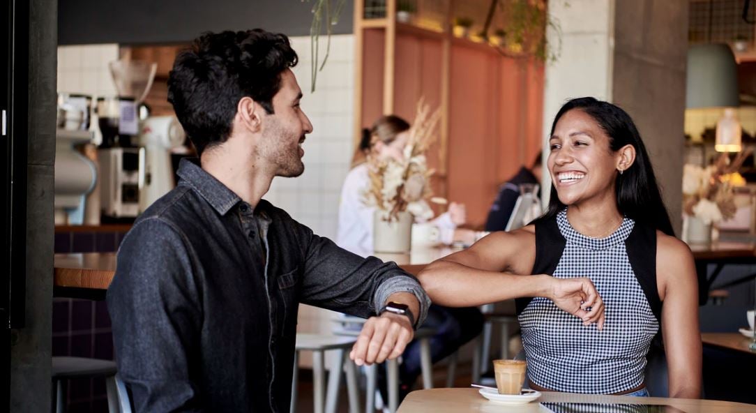Man en vrouw in een cafe begroeten elkaar met hun ellebogen