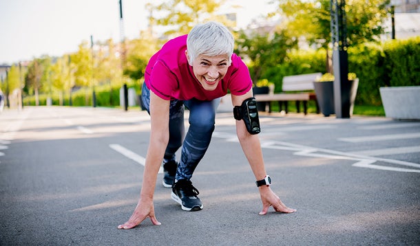 Een sportieve, oudere vrouw in hardloopkleding staat klaar om te gaan sprinten op de openbare weg
