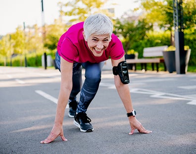  A sporty elderly woman in running clothes is ready to sprint on the open road