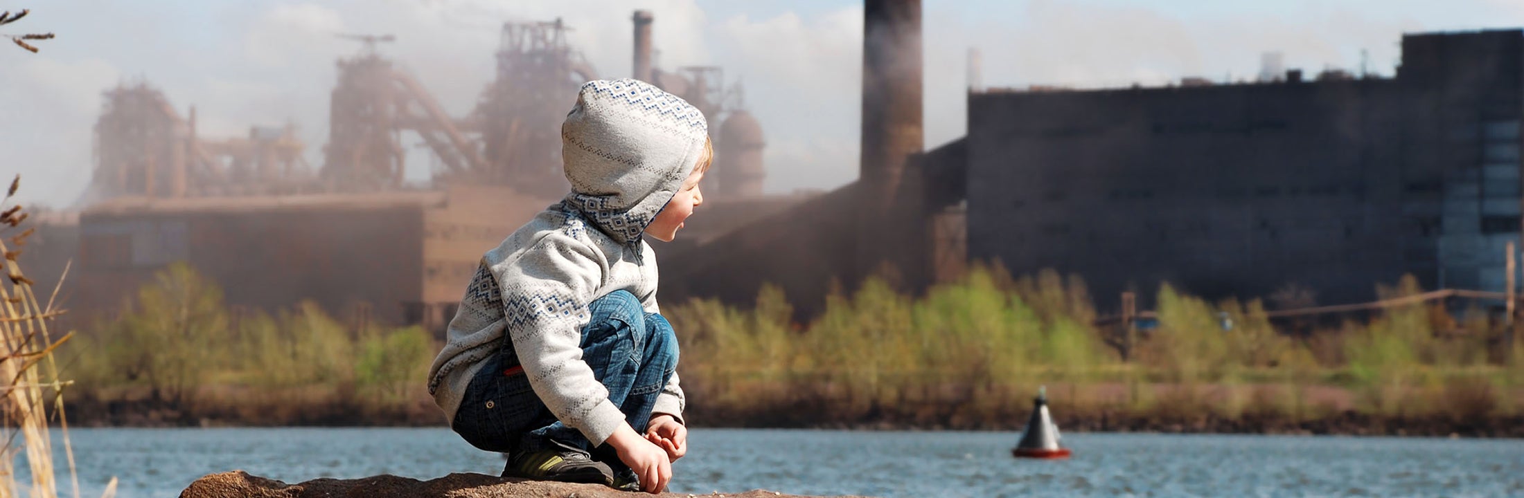 Kind zit naast een rivier vlakbij een fabriek