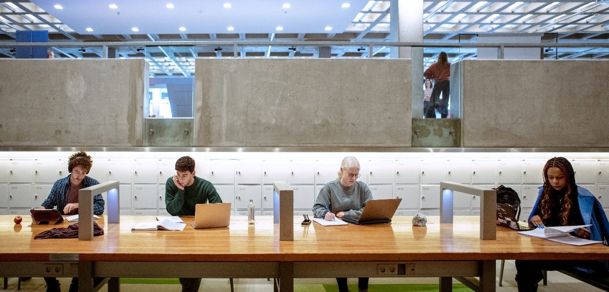 Mensen studeren aan bureaus in een openbare ruimte in het hoofdgebouw van de Vrije Universiteit Amsterdam. 